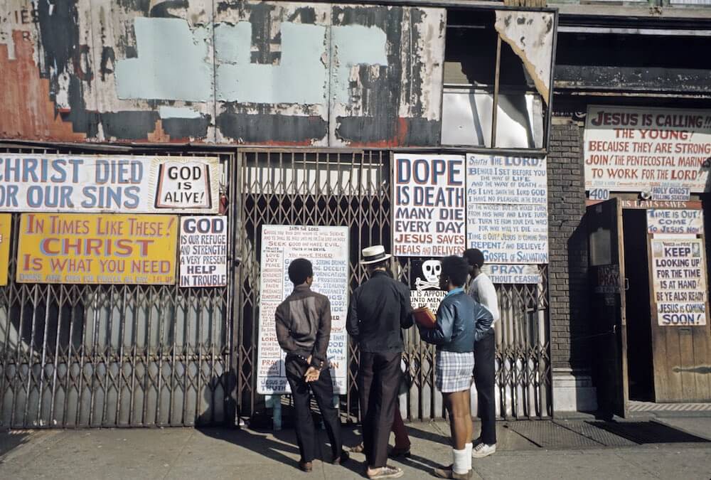 Harlem: The Ghetto. New York City- Harlem- juillet 1970: le ghetto; trois enfants lisent les affiches de propagande pentecÙtiste placardÈes sur un rez-de-chaussÈe d'immeuble et prÙnant l'arrÍt de la drogue. (Photo by Jack Garofalo/Paris Match via Getty Images)