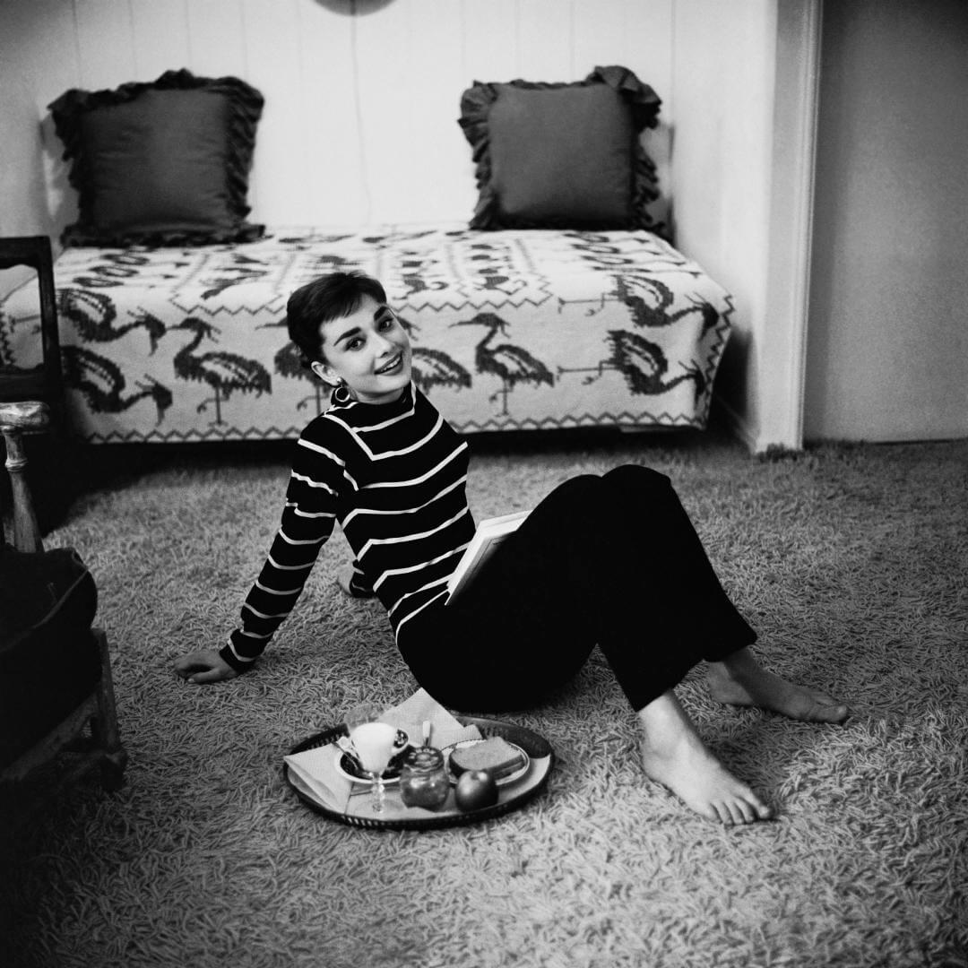 Audrey Hepburn sentada y sonriendo en la alfombra de su casa