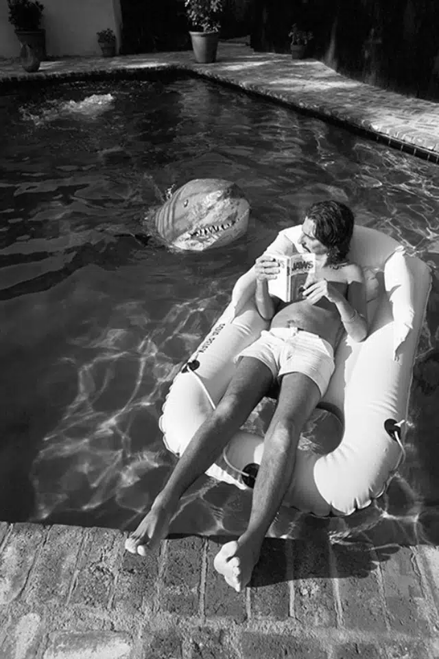 Alice Cooper en la piscina leyendo junto a un tiburon