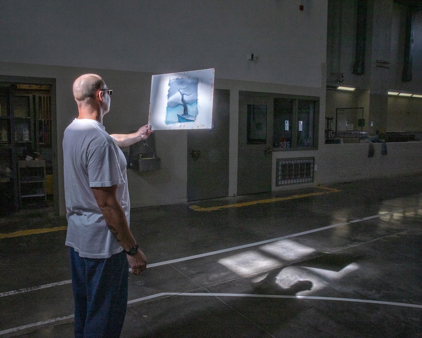 A student stops to inspect his painting in window light, in a gym at Pleasant Valley State Prison.